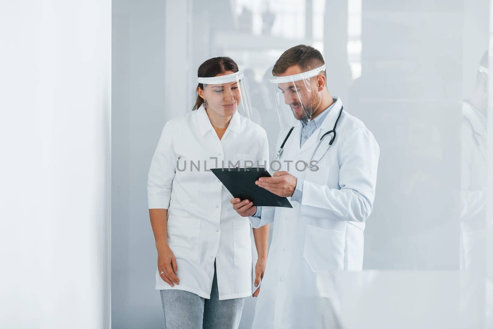 In protective masks. Two doctors in white coats is in the clinic working together.