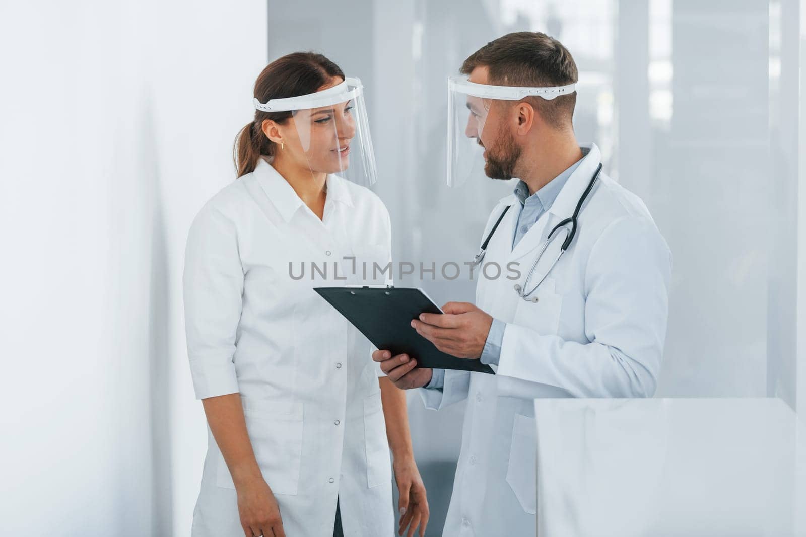 In protective masks. Two doctors in white coats is in the clinic working together.