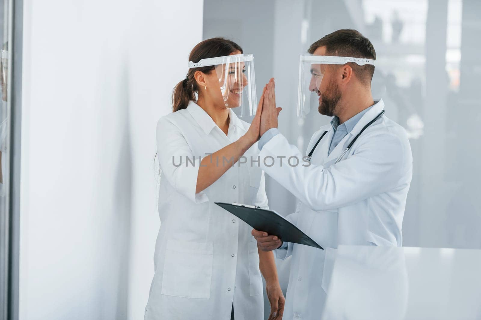 In protective masks. Two doctors in white coats is in the clinic working together.