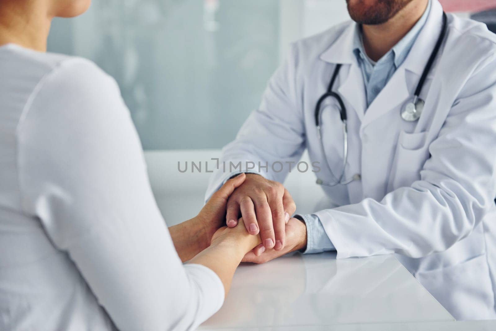 Holding patient by hands. Professional medic in white coat is in the clinic.