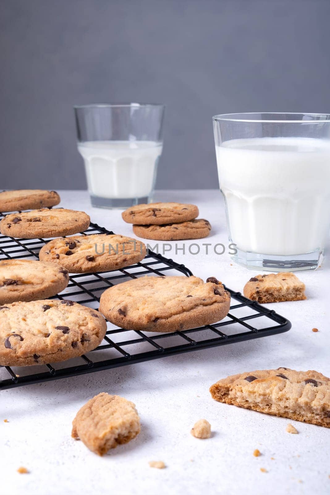 Close-up of baked oatmeal cookies with chocolate chips on a metal cooling rack and milk in a glass. Selective focus. Vertical orientation.