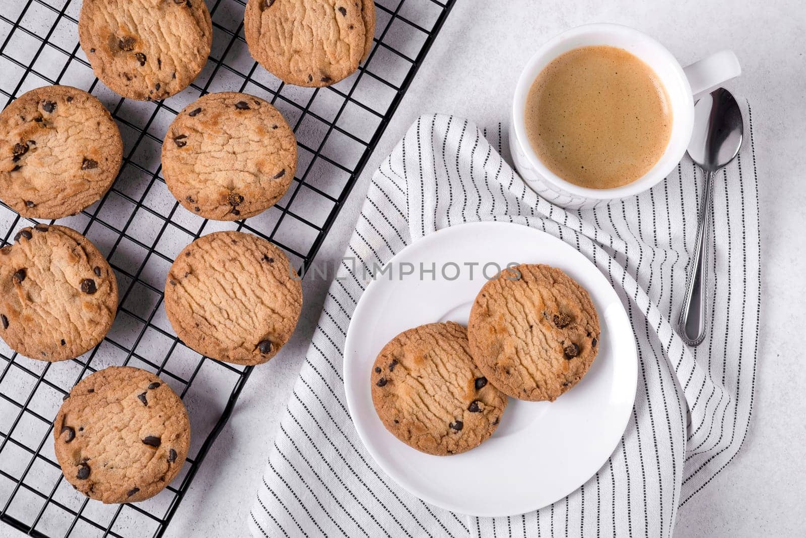 Close-up of baked oatmeal cookies with chocolate chips on a metal cooling rack and coffee in a white porcelain mug. Selective focus.