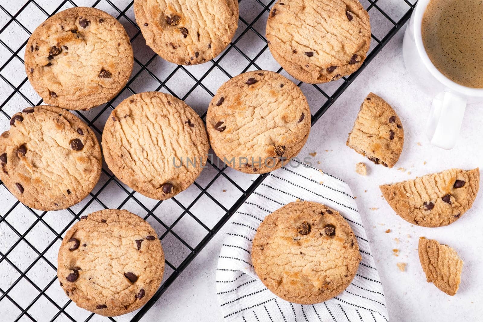 Close-up of baked oatmeal cookies with chocolate chips on a metal cooling rack and coffee in a white porcelain mug. Selective focus.