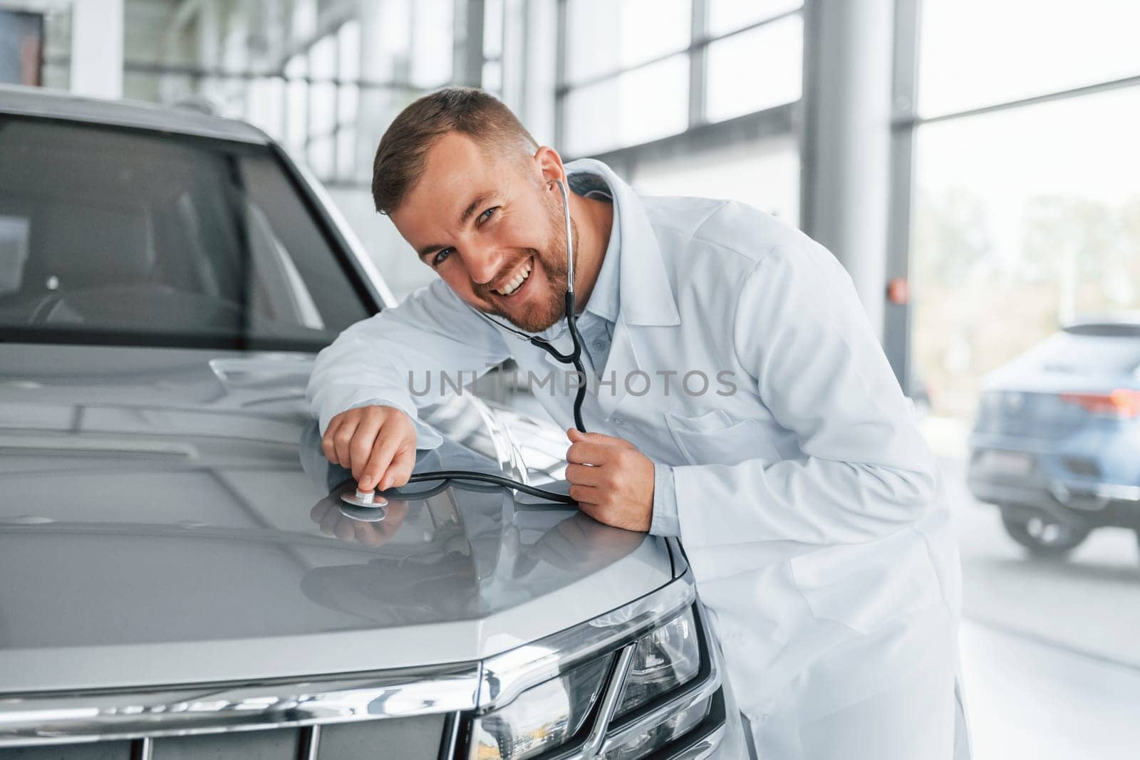 Medic in white coat is using stethoscope on the automobile.