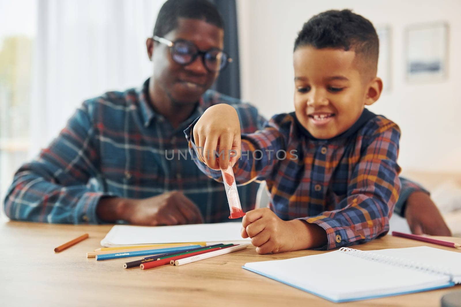 Sitting by the table with laptop. African american father with his young son at home.