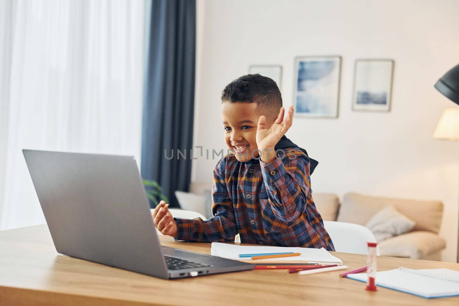 With laptop. Cheerful young boy is at home alone.