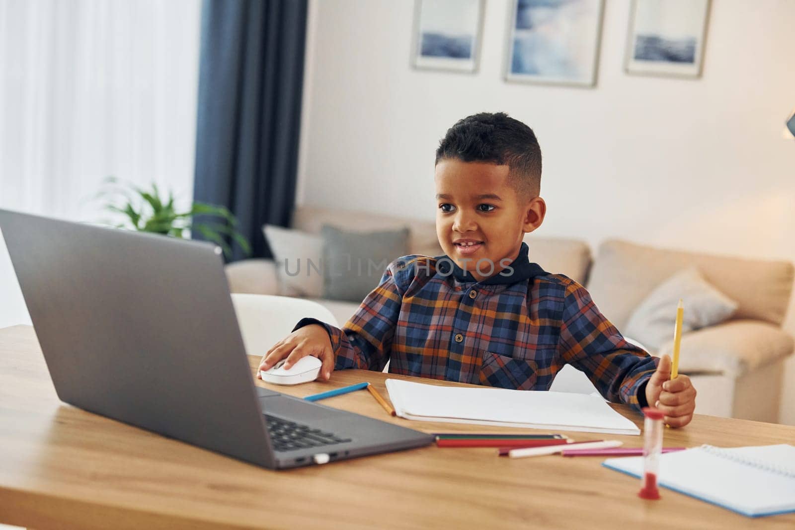 With laptop. Cheerful young boy is at home alone.