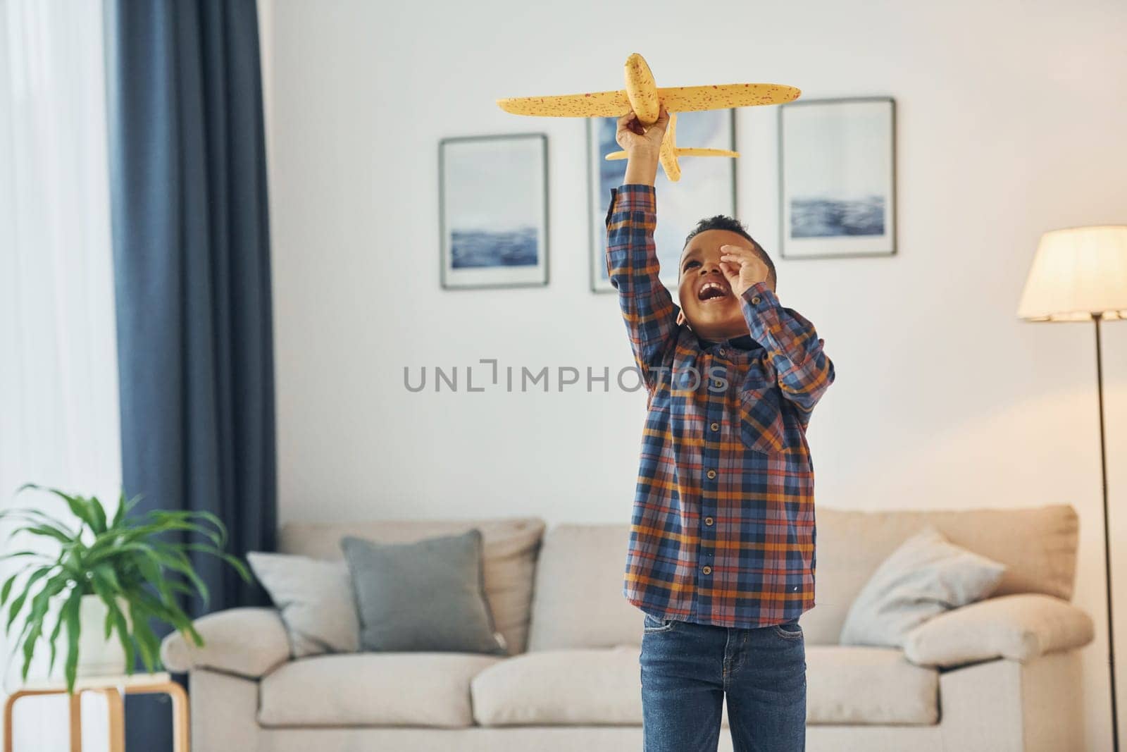 Playing with yellow toy plane. Cheerful young boy is at home alone.