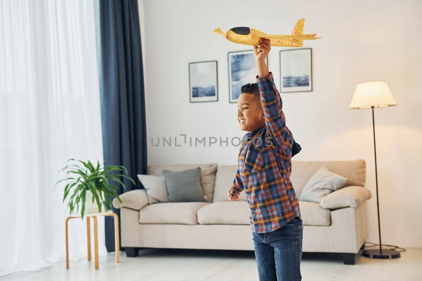 Playing with yellow toy plane. Cheerful young boy is at home alone.