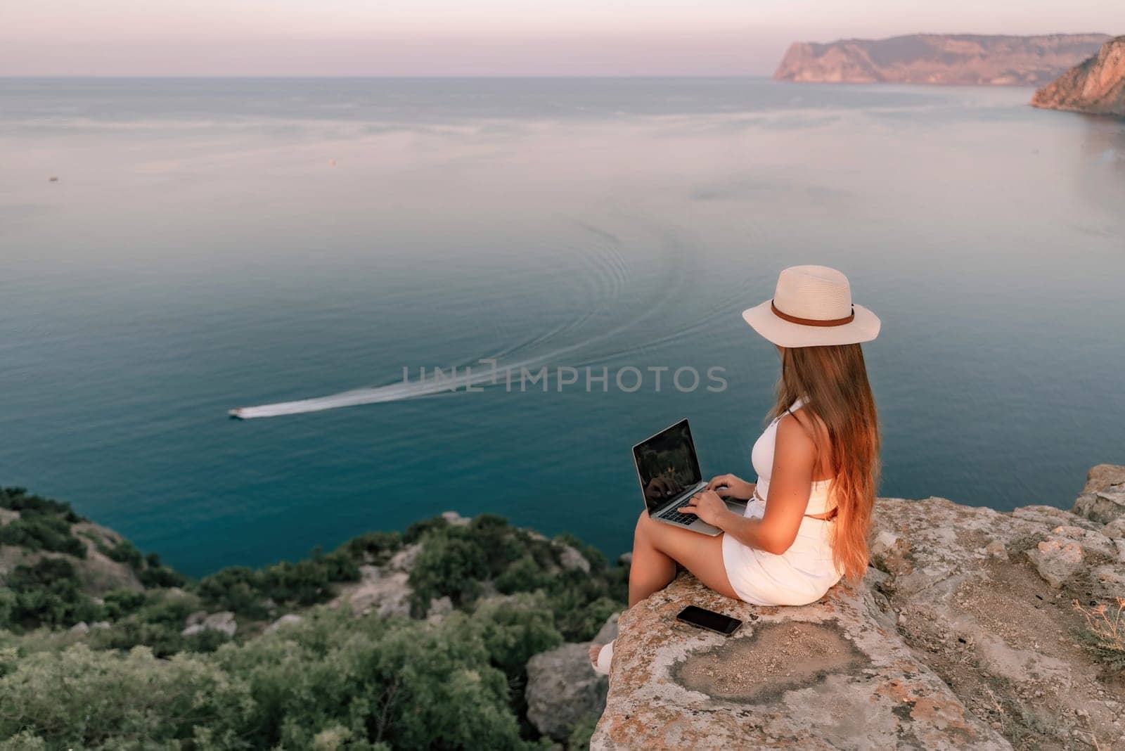 Freelance women sea working on the computer. Good looking middle aged woman typing on a laptop keyboard outdoors with a beautiful sea view. The concept of remote work. by Matiunina