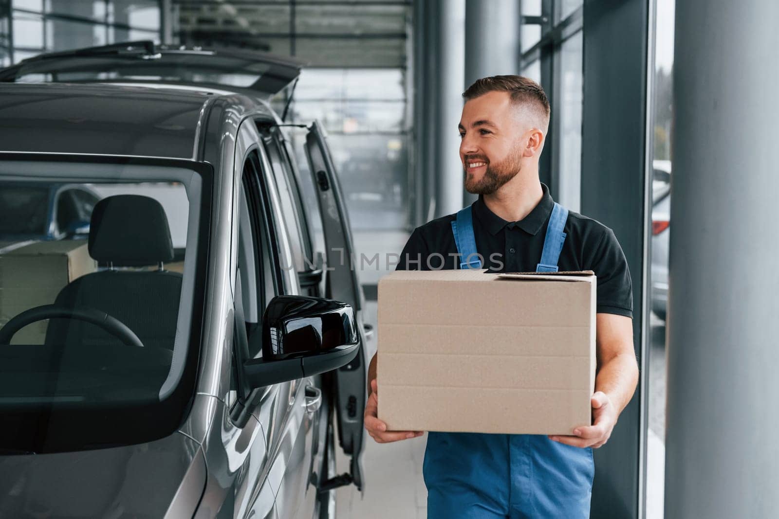 Paper box. Delivery man in uniform is indoors with car and with order.