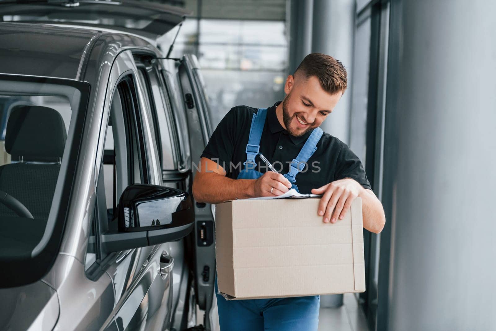 Paper box. Delivery man in uniform is indoors with car and with order.