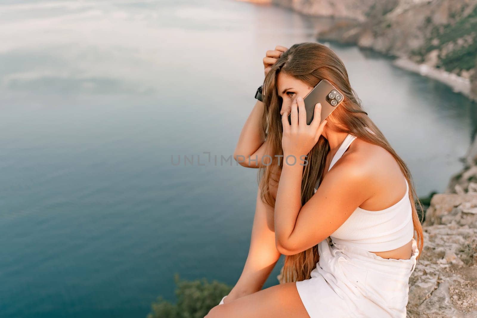 Sea phone Portrait of a happy woman on the background of the sea, dressed in white shorts and a T-shirt, long hair loose, talking on the phone.