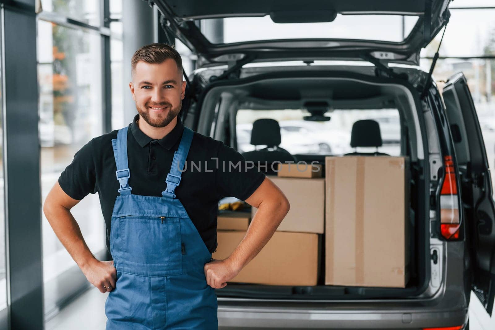 Portrait of delivery man in uniform that is indoors with car and with order.