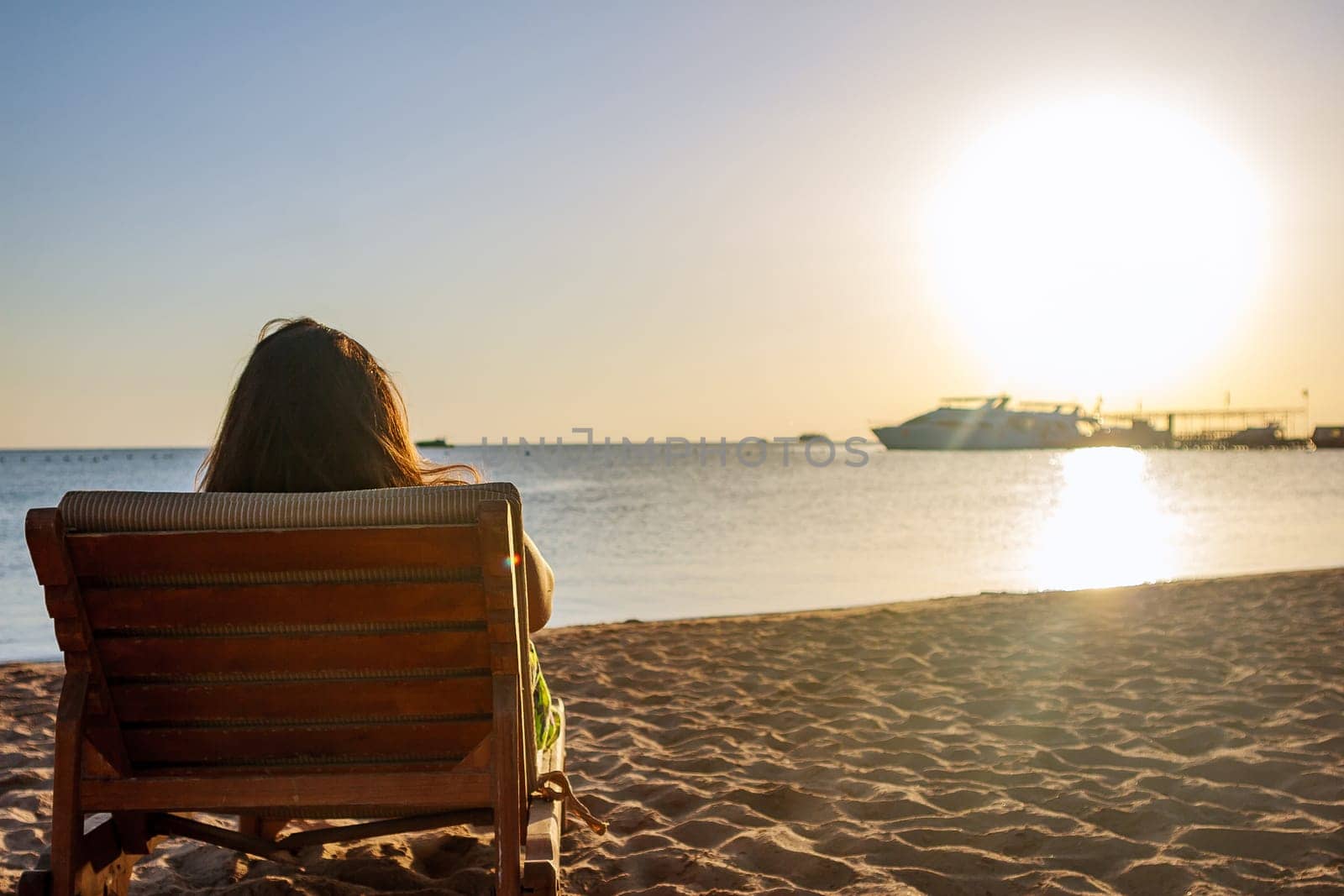 Young woman relaxing in a deck chair on the beach in the morning, meeting the dawn.