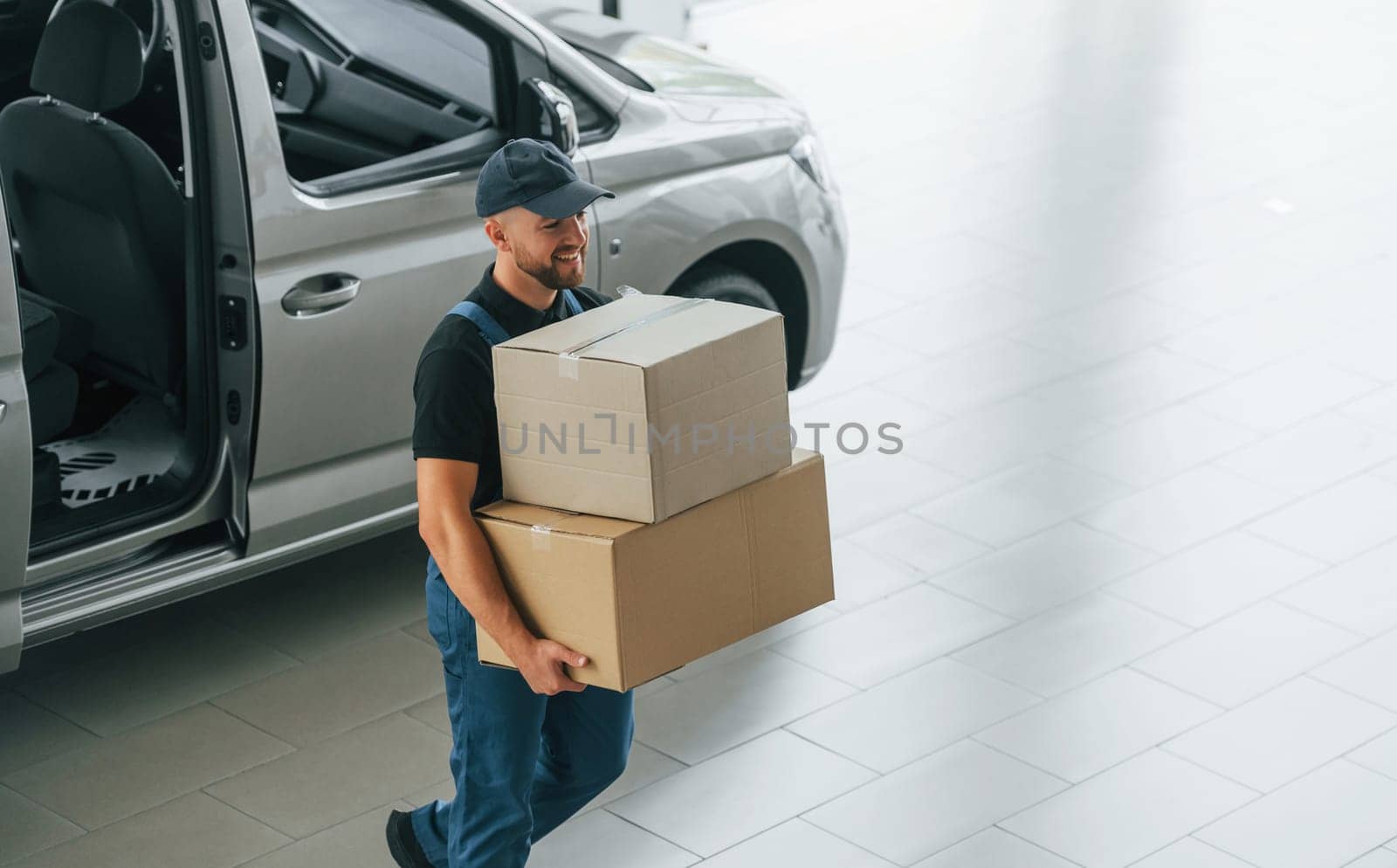 Business of service. Delivery man in uniform is indoors with car and with order.