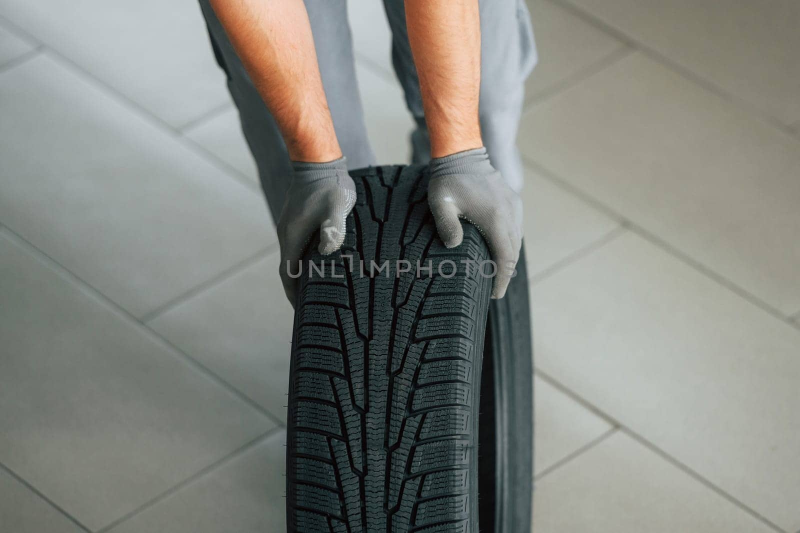 Installing new tire. Man in uniform is working in the autosalon at daytime.