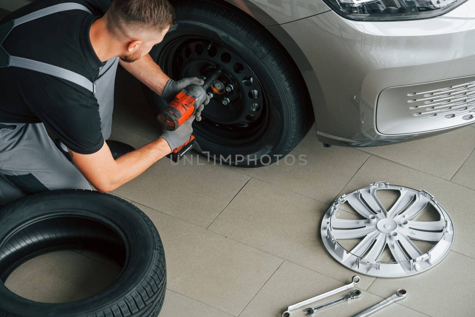 Installing new tire. Man in uniform is working in the autosalon at daytime.