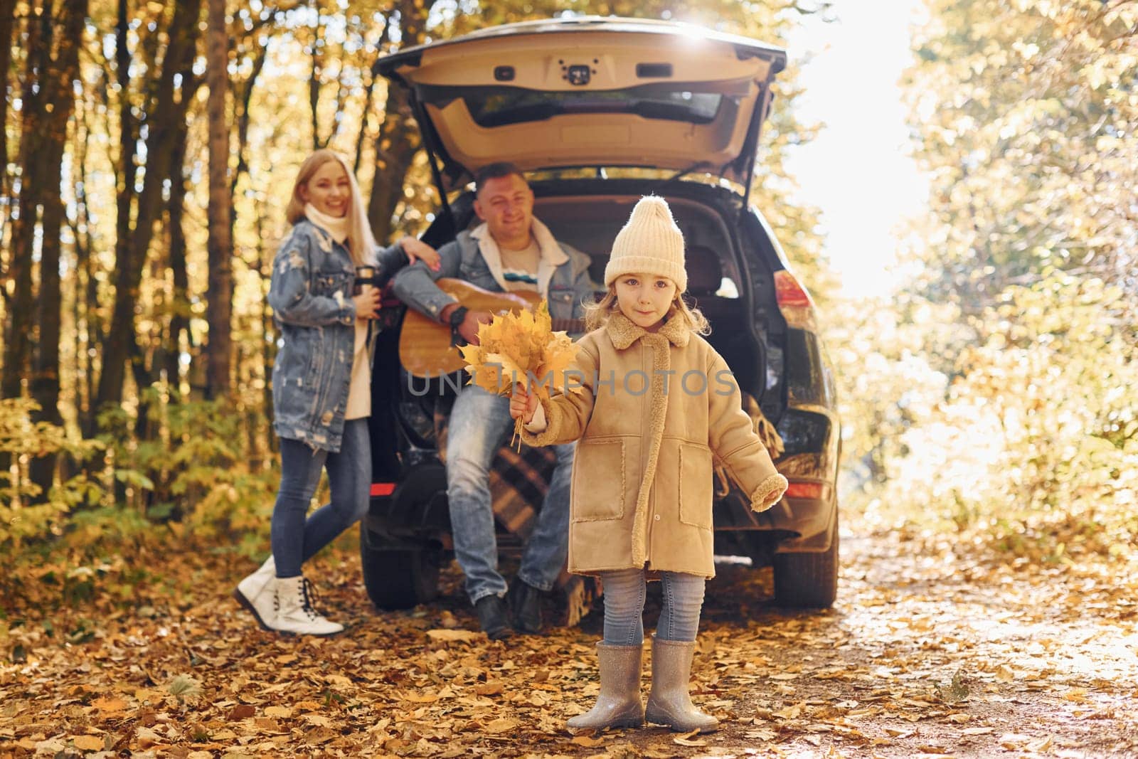 With acoustic guitar. Happy family is in the park at autumn time together.