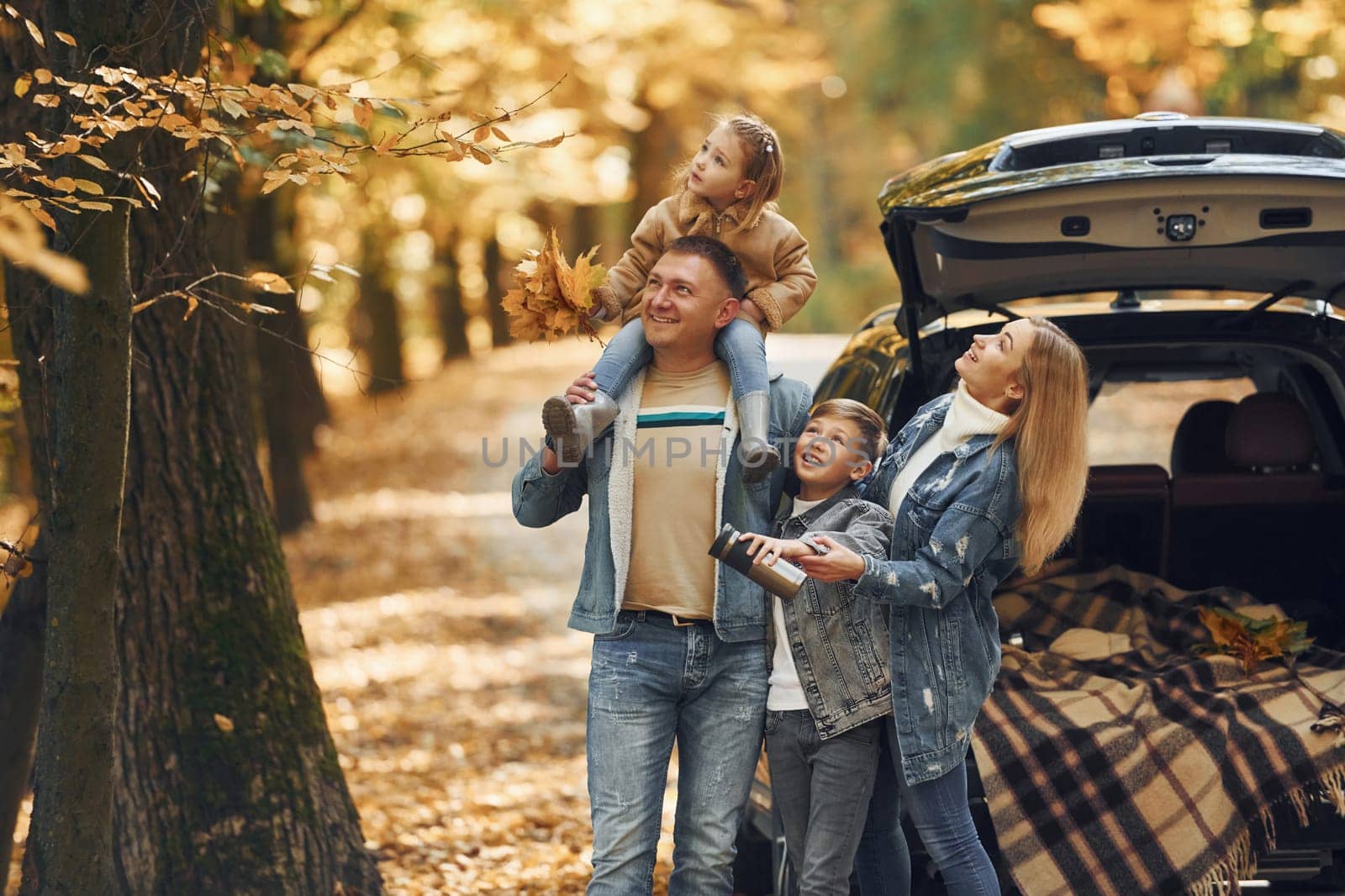 Near car with open trunk. Happy family is in the park at autumn time together.