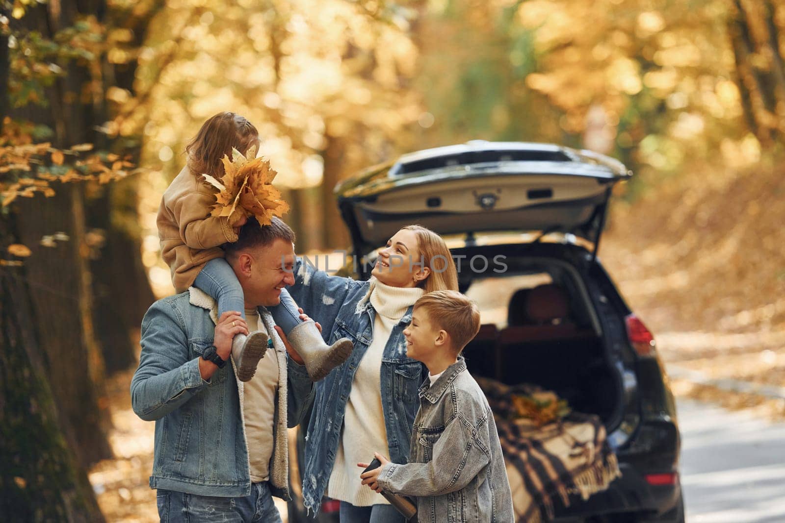 Near car with open trunk. Happy family is in the park at autumn time together.