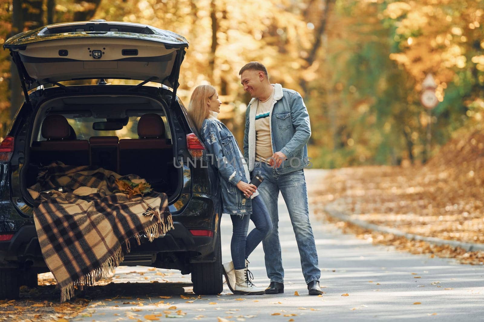 Opened trunk. Couple standing on the road in park near automobile.