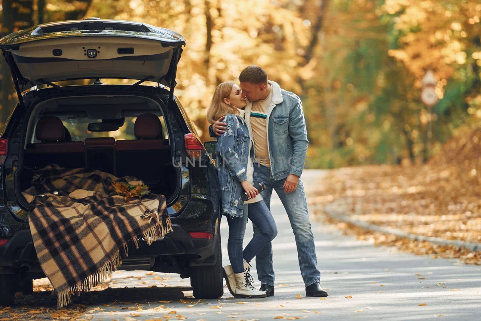 Opened trunk. Couple standing on the road in park near automobile.