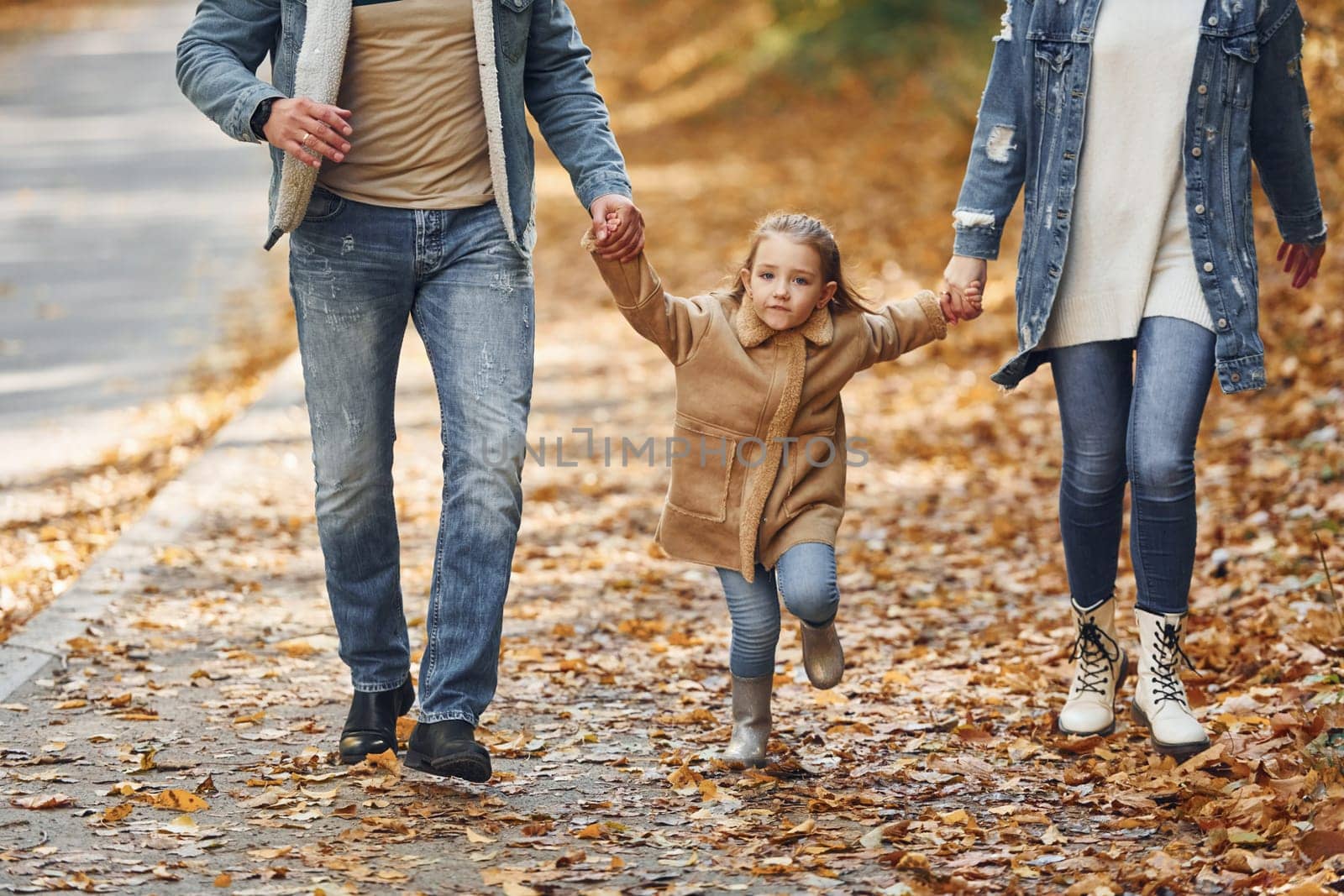 Holding daughter by hands. Happy family is in the park at autumn time together.