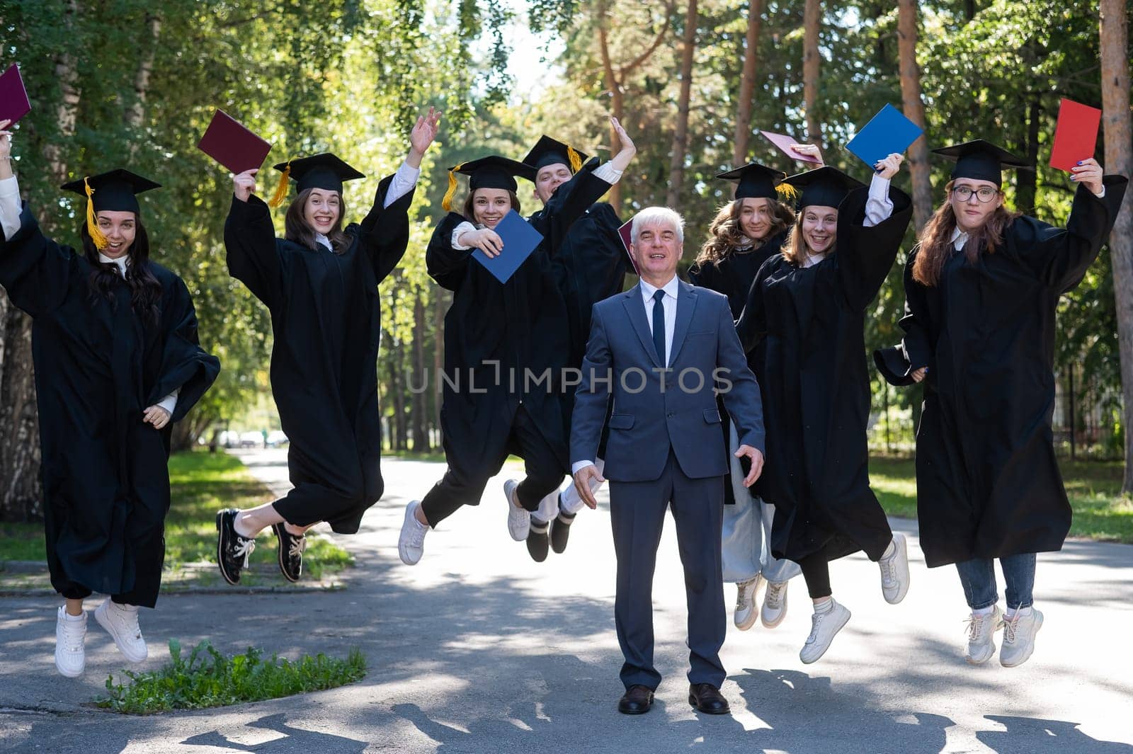 A university professor and seven robed graduates are jumping outdoors. by mrwed54