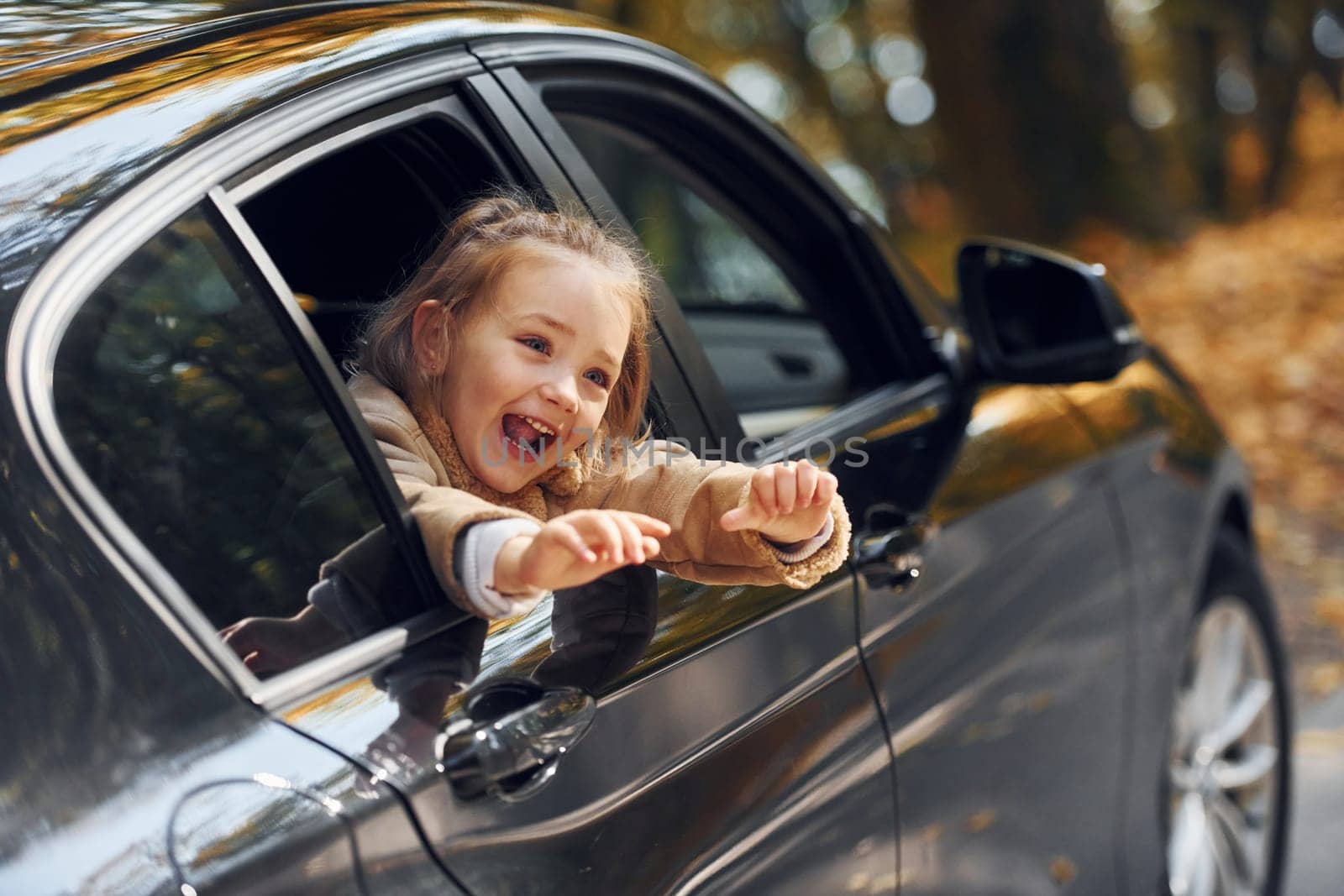 Little girl sitting in the black automobile and looking through the window.