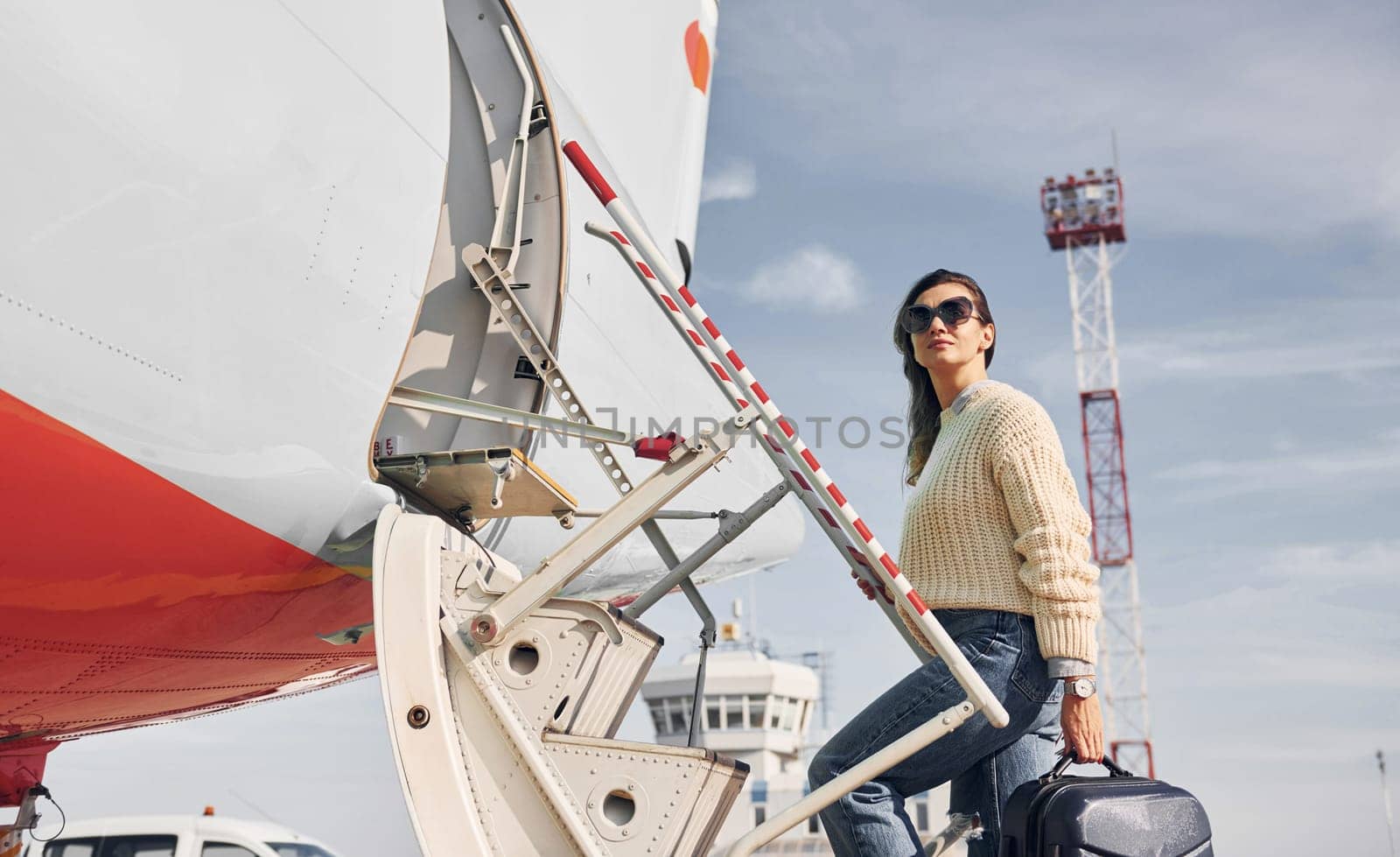 With lugagge. Young female passanger in casual clothes is outdoors near the plane.