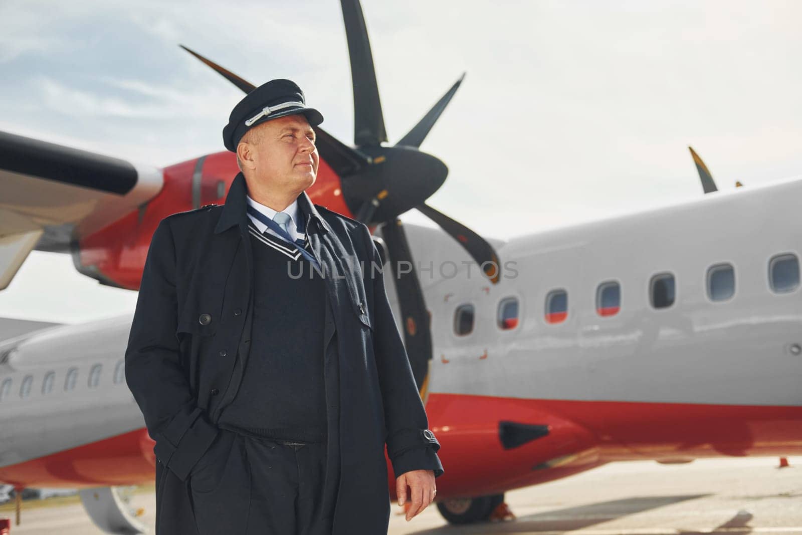 Pilot in formal black uniform is standing outdoors near plane.