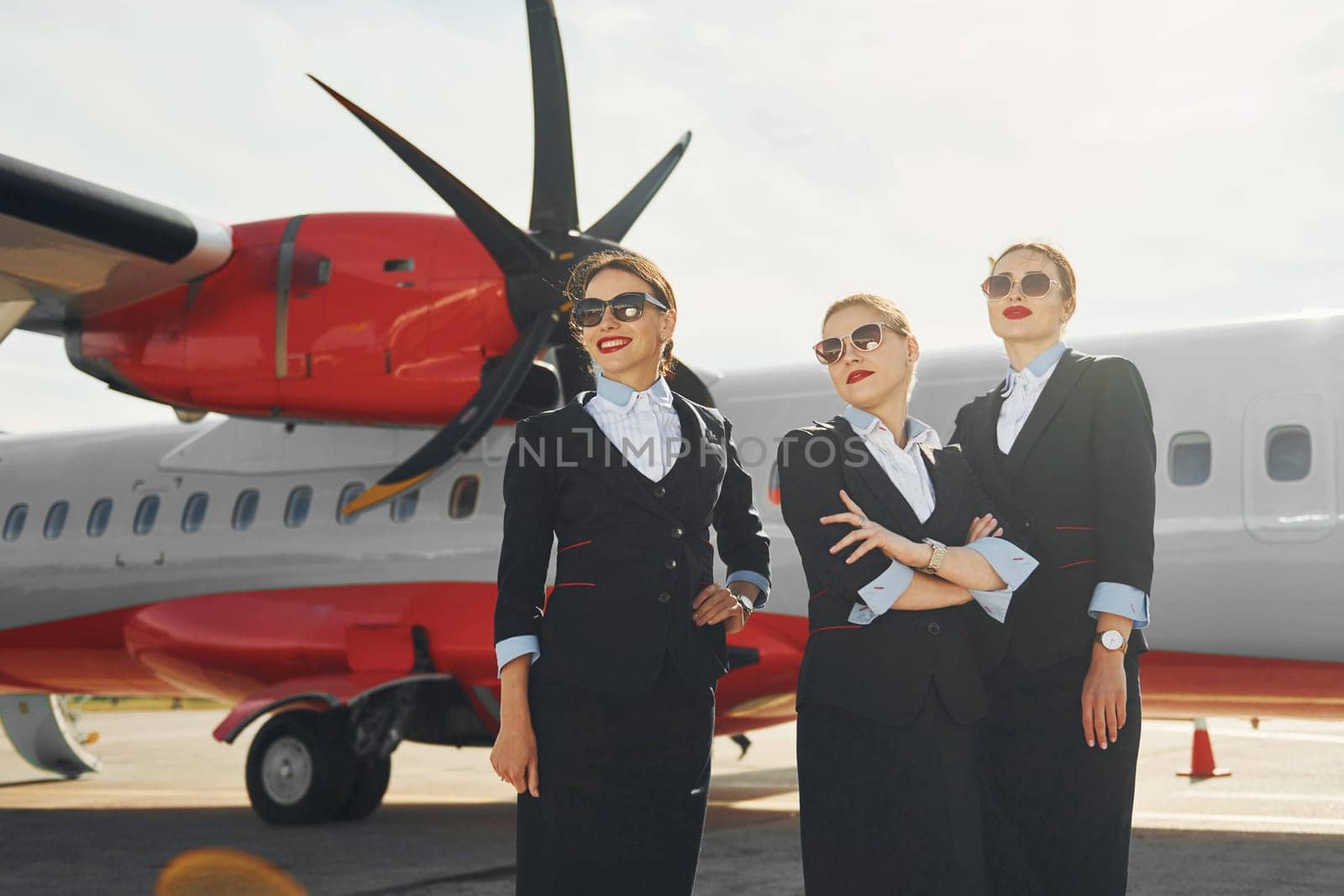 Three stewardesses. Crew of airport and plane workers in formal clothes standing outdoors together.