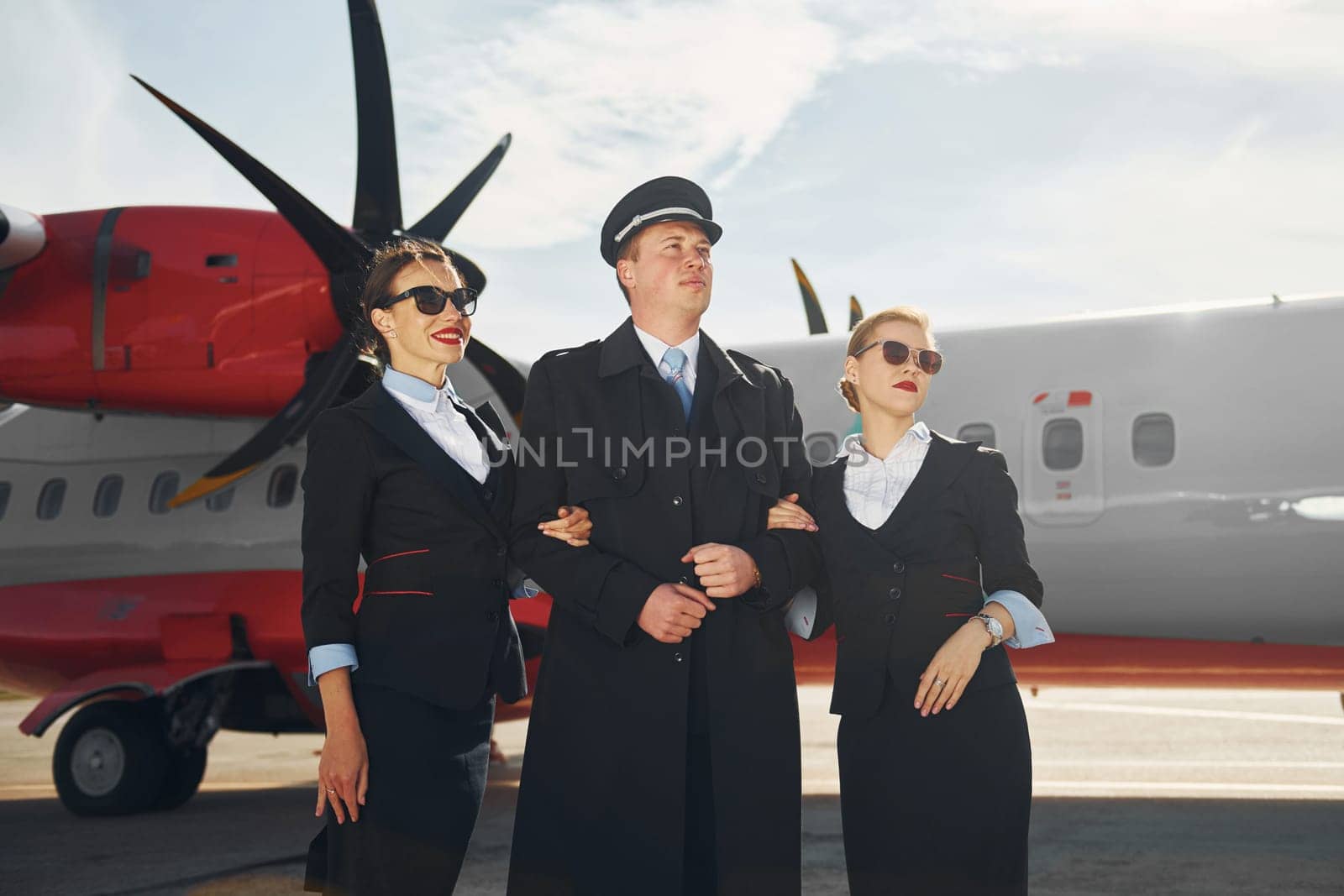 Three people. Crew of airport and plane workers in formal clothes standing outdoors together.