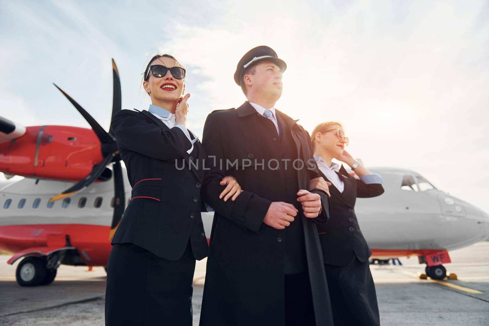 Three people. Crew of airport and plane workers in formal clothes standing outdoors together.