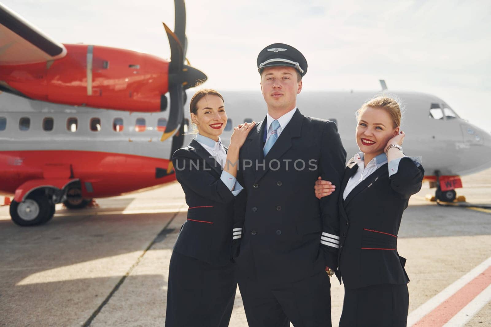 Pilot and two stewardesses. Crew of airport and plane workers in formal clothes standing outdoors together.