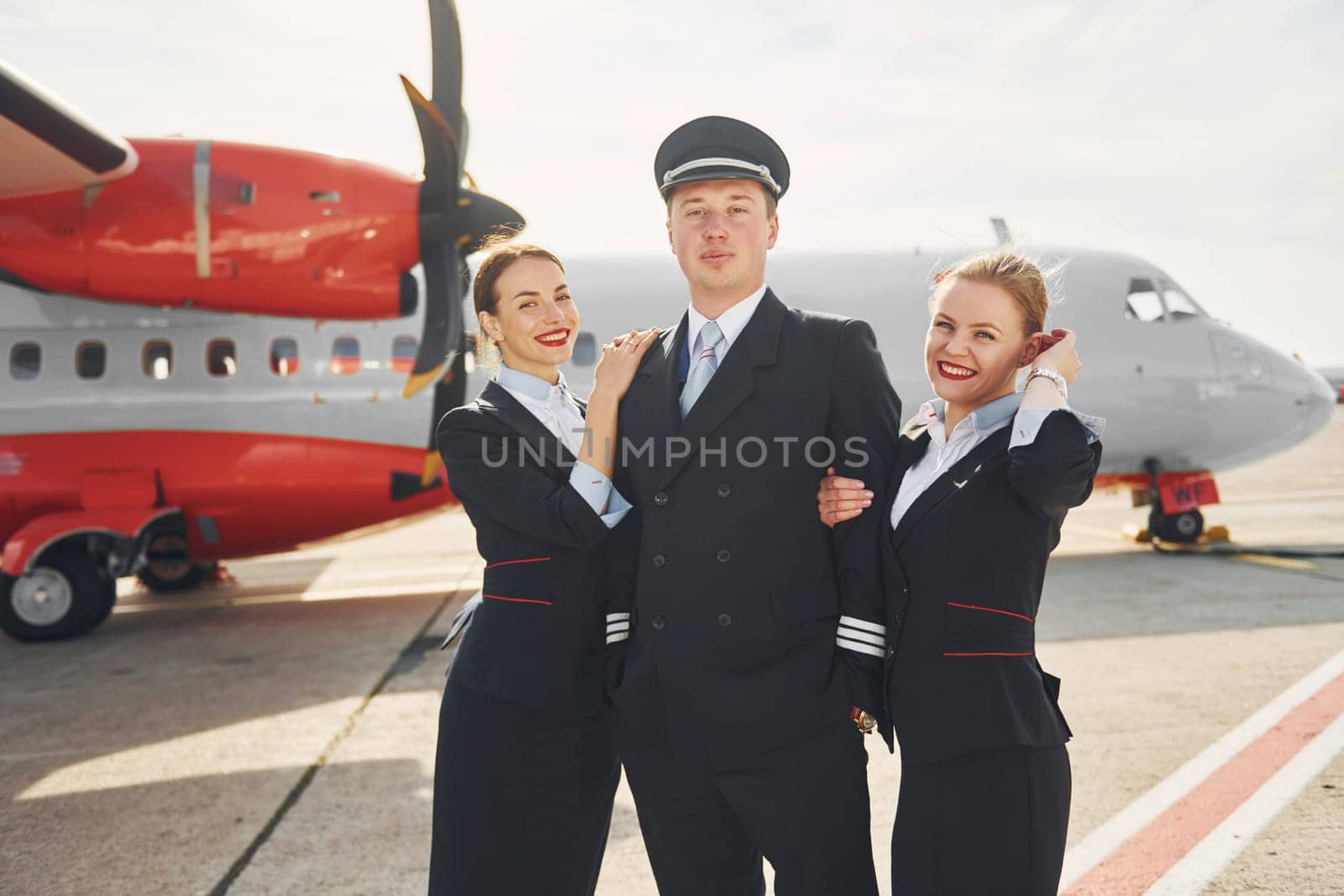Pilot and two stewardesses. Crew of airport and plane workers in formal clothes standing outdoors together.