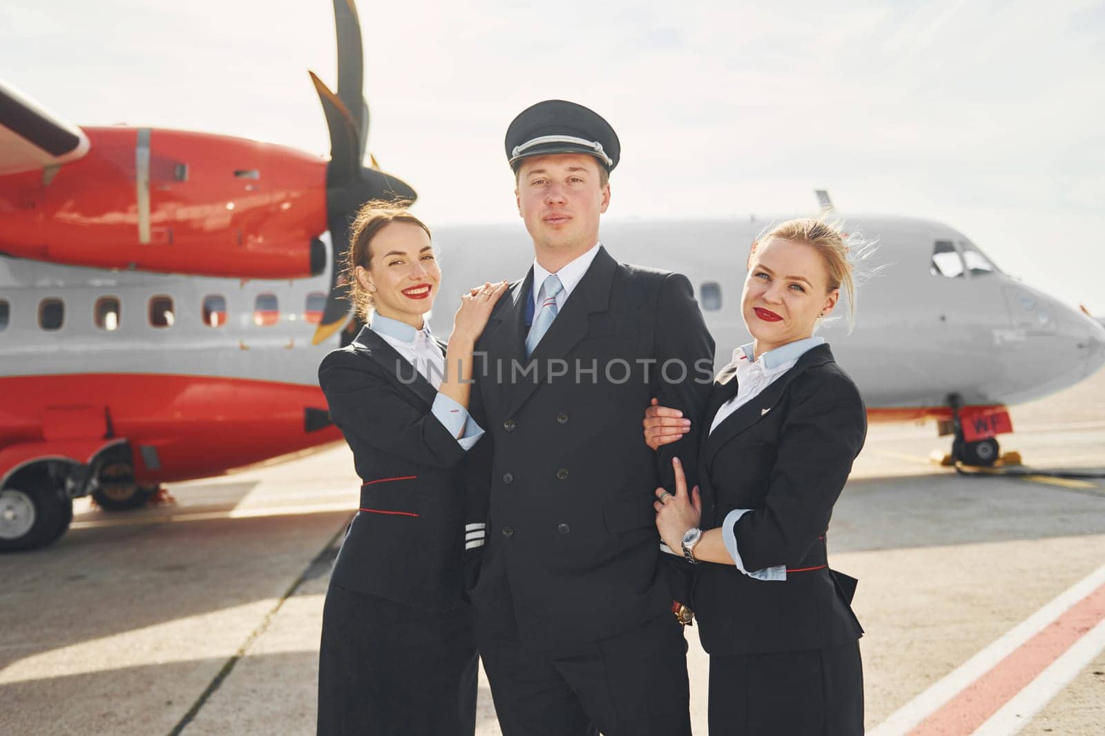 Pilot and two stewardesses. Crew of airport and plane workers in formal clothes standing outdoors together.