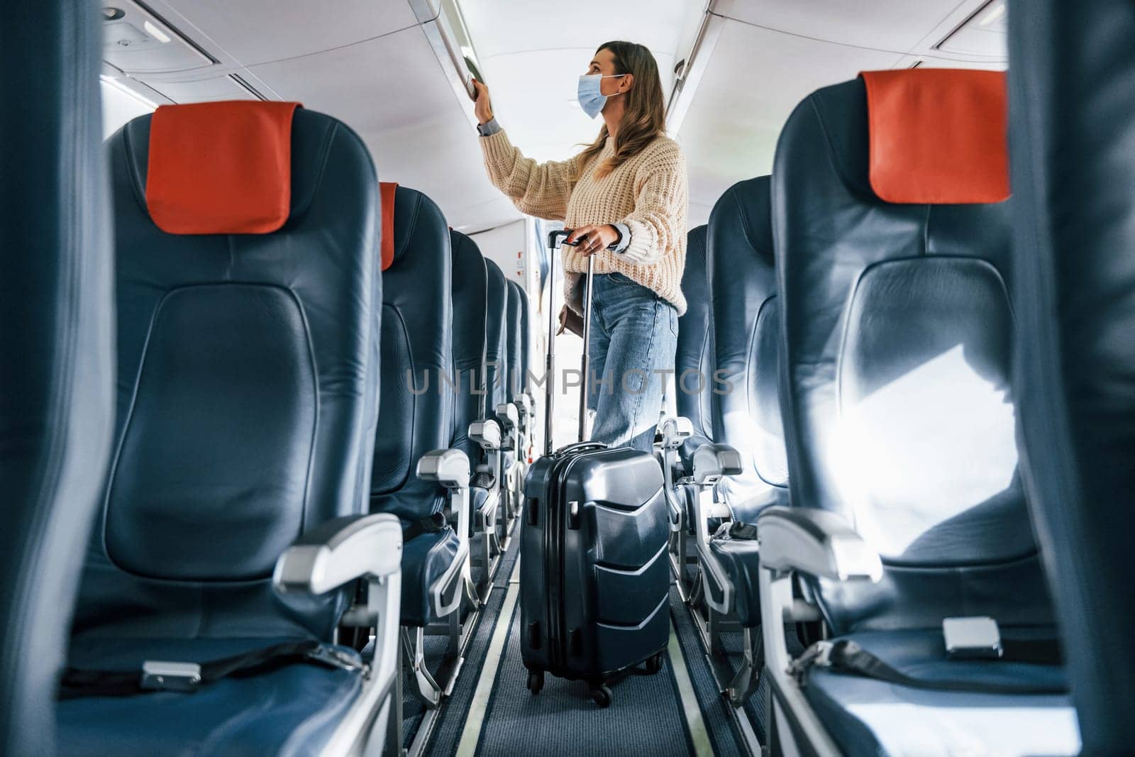 With lugagge. Young female passanger in casual clothes is in the plane.
