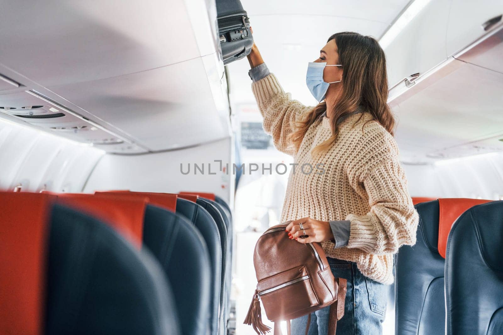With lugagge. Young female passanger in casual clothes is in the plane.