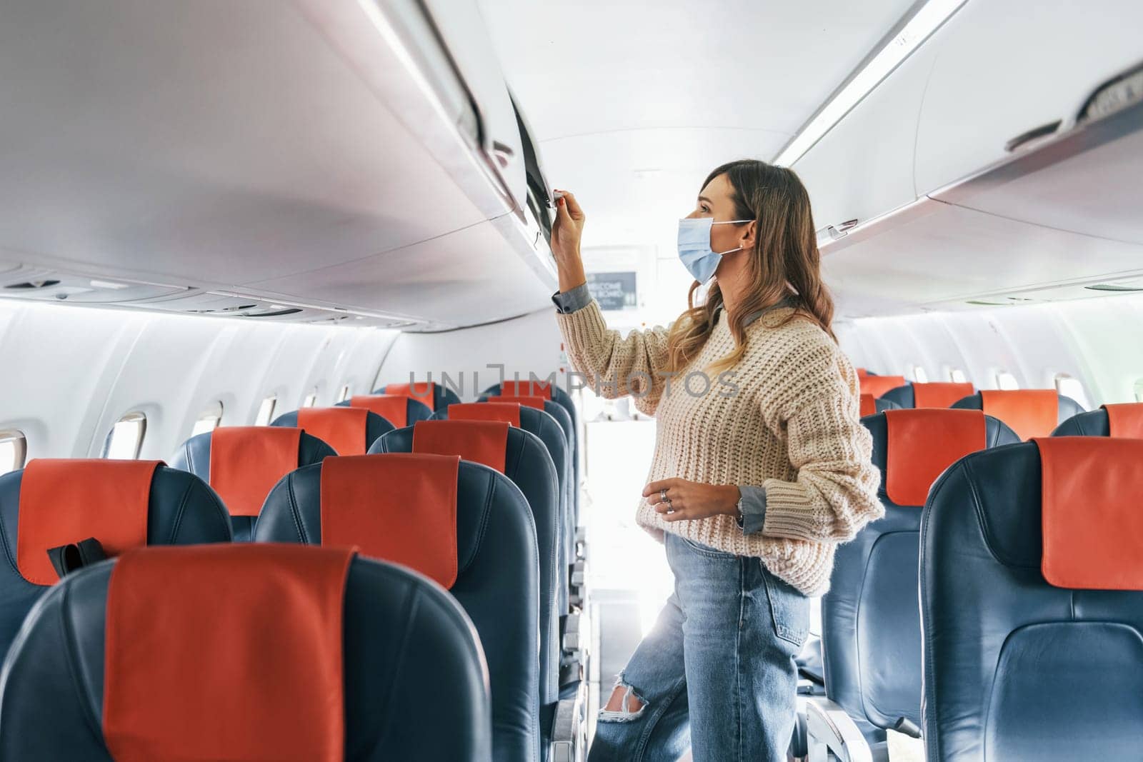 With lugagge. Young female passanger in casual clothes is in the plane.