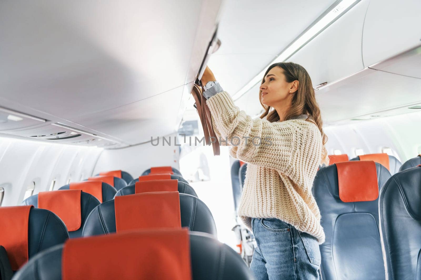 Holding lugagge. Young female passanger in casual clothes is in the plane.