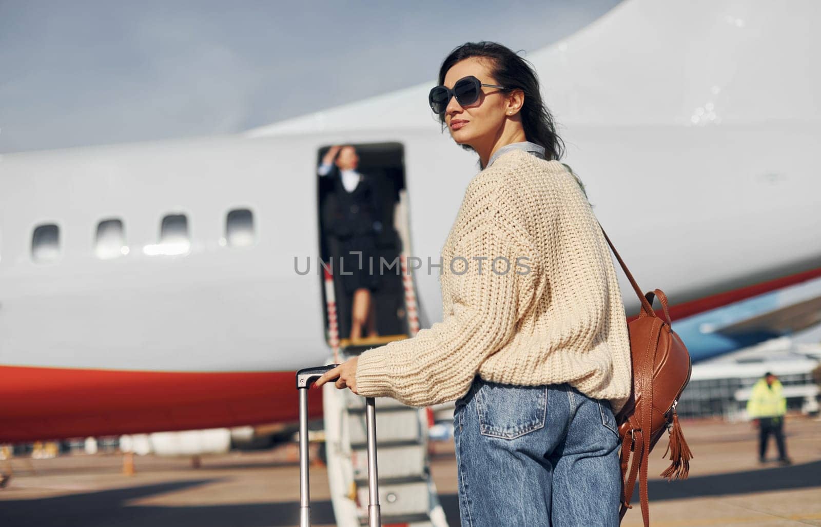 At daytime. Young female passanger in casual clothes is outdoors near the plane.
