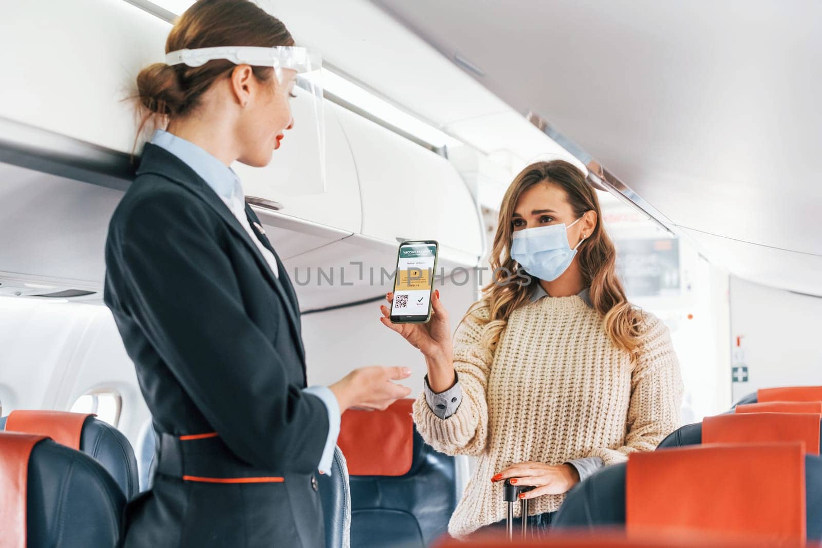Showing COVID-19 vaccine sertificate to stewardess. Young female passanger in casual clothes is in the plane.