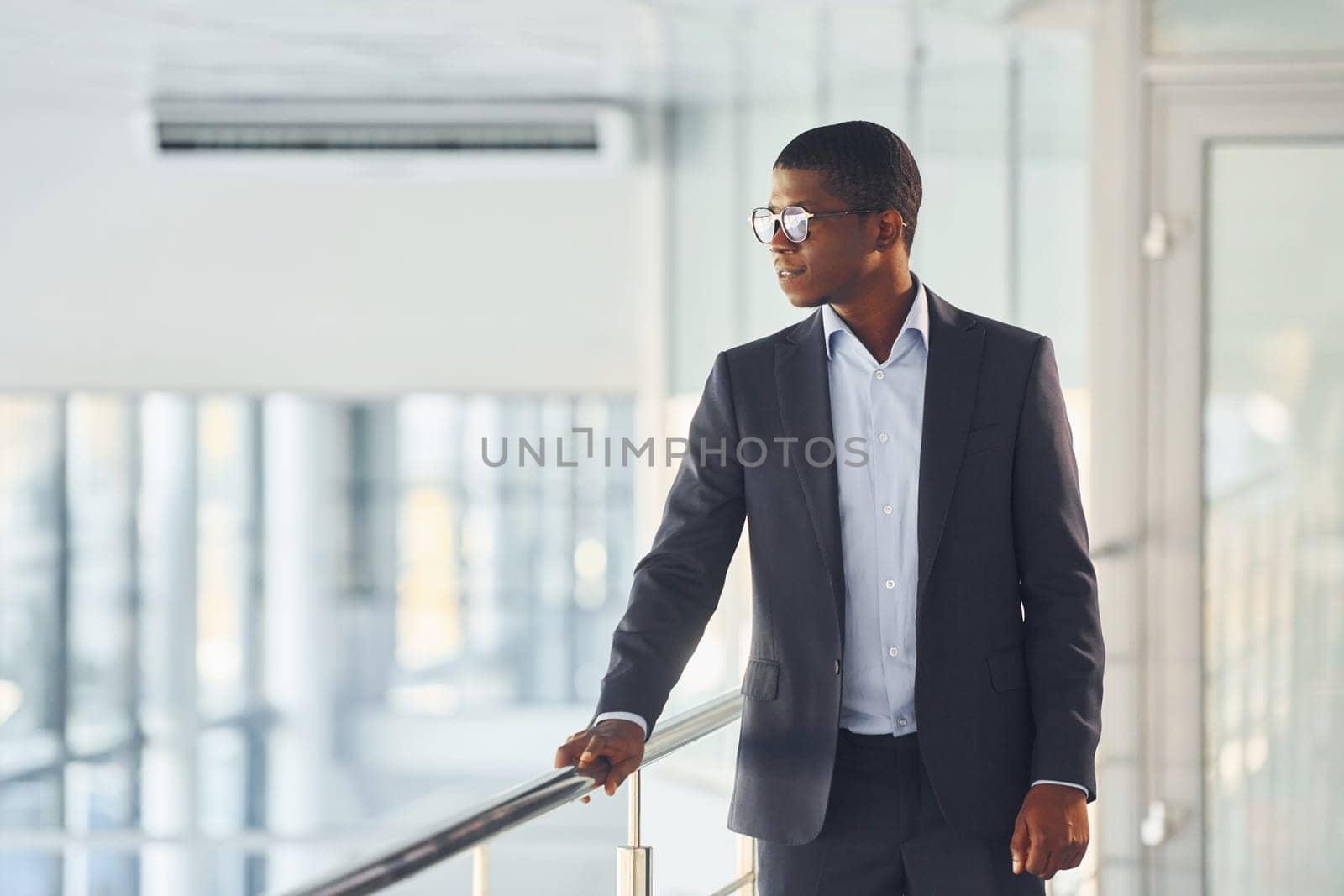 Leaning on the railings. Young african american businessman in black suit is indoors.