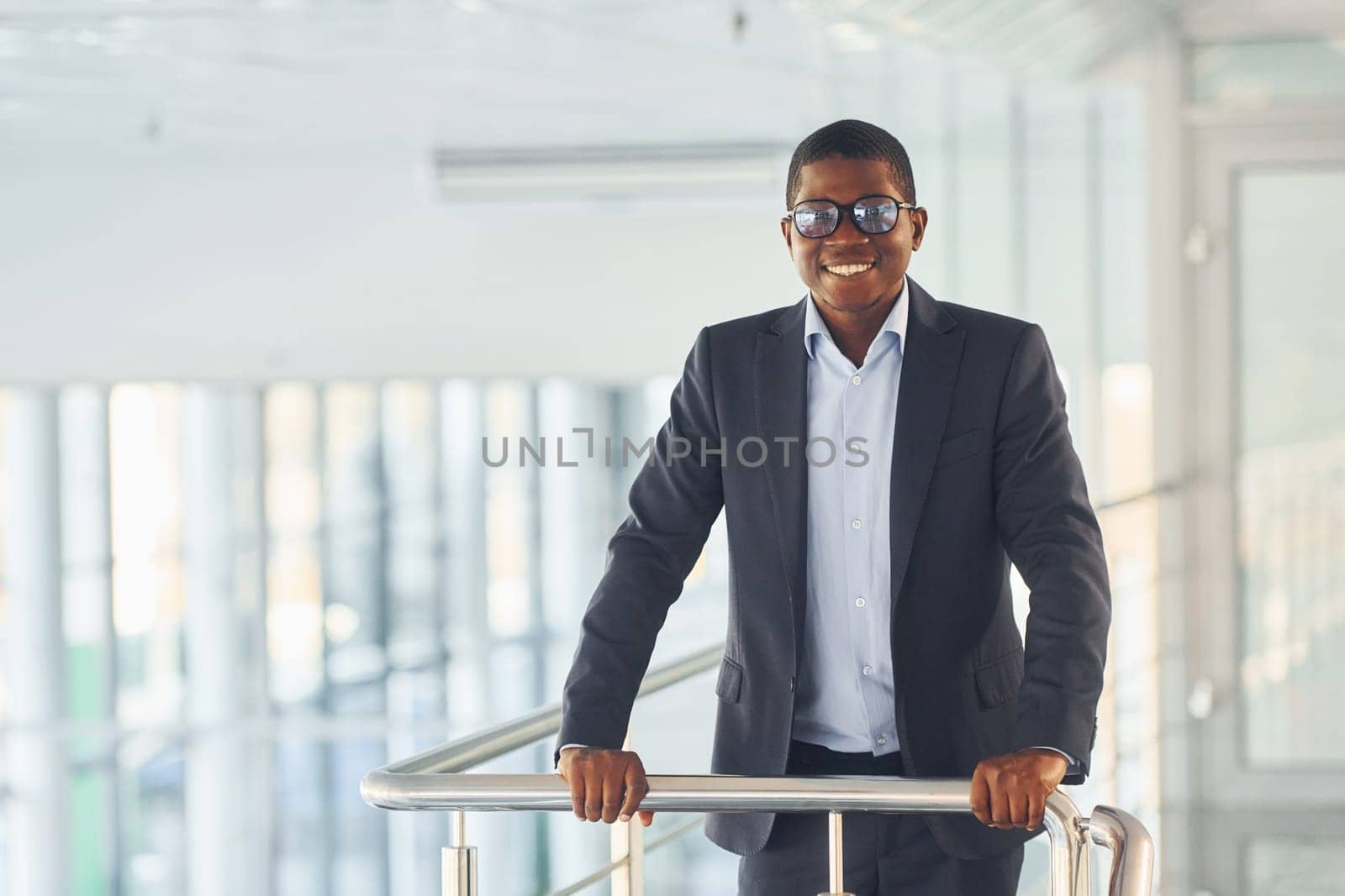 Leaning on the railings. Young african american businessman in black suit is indoors.
