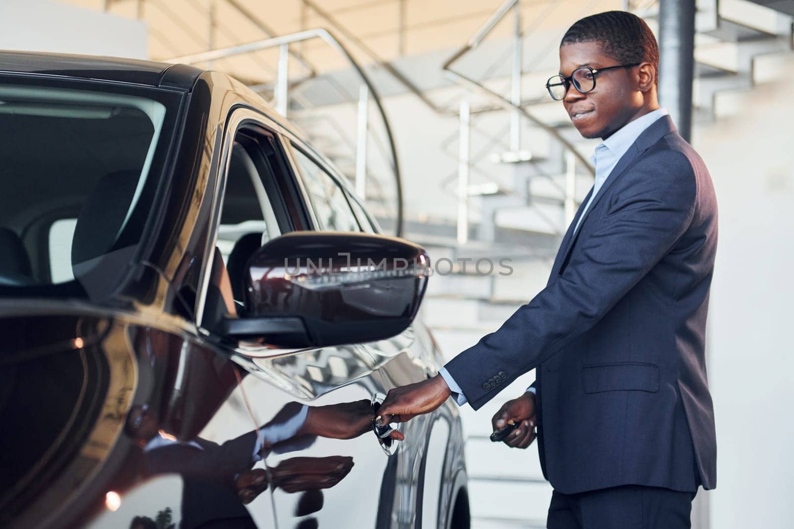 Opening the door. Young african american businessman in black suit is the autosalon.