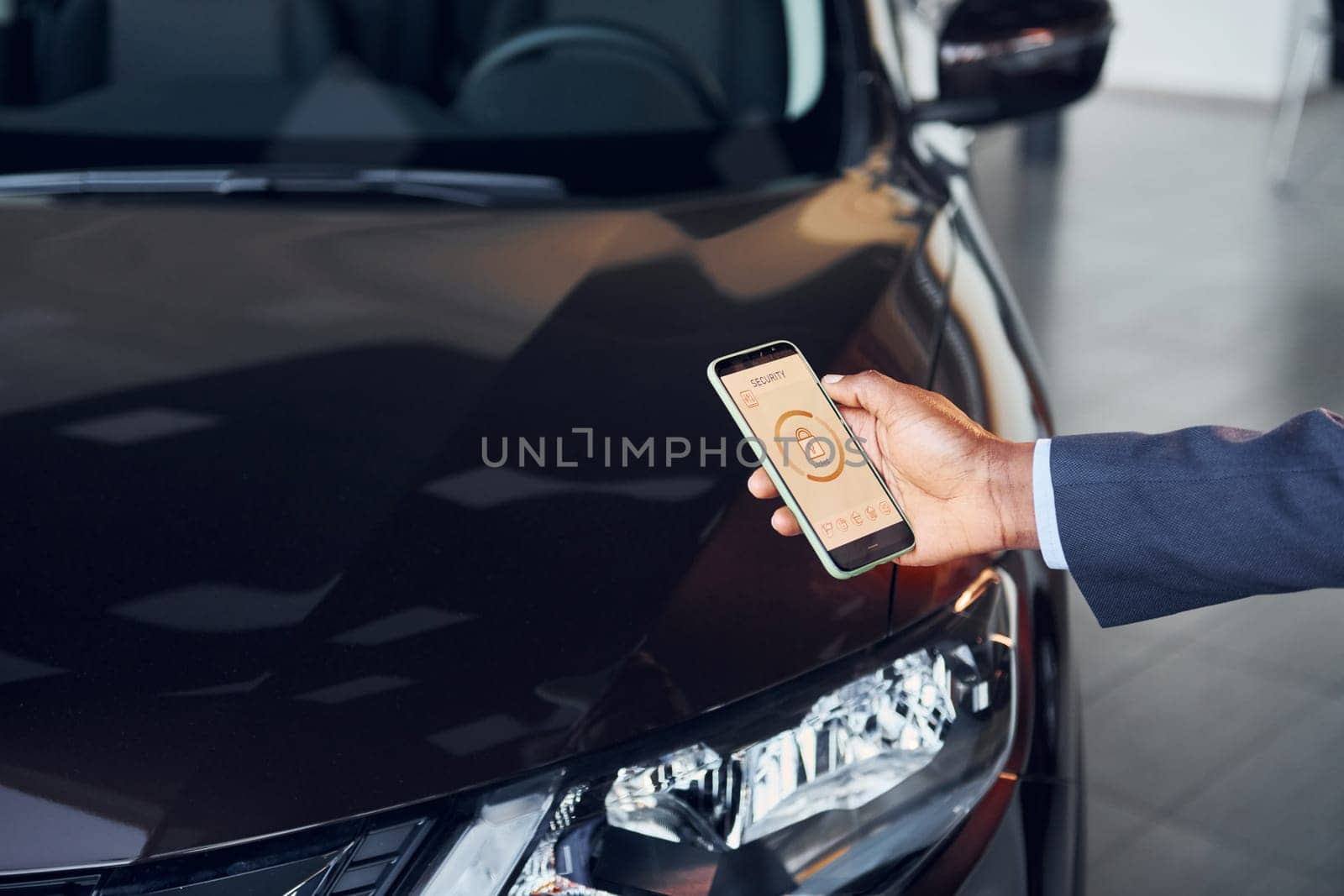 Using smartphone to open door. Young african american businessman in black suit is the autosalon.