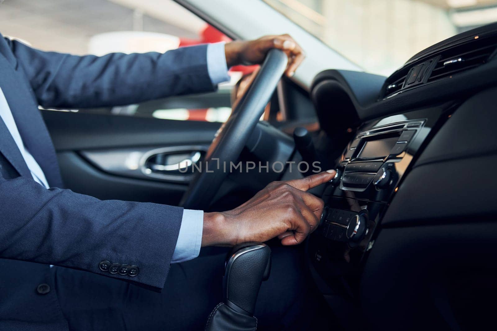 Side view. Young african american businessman in black suit is in the automobile.