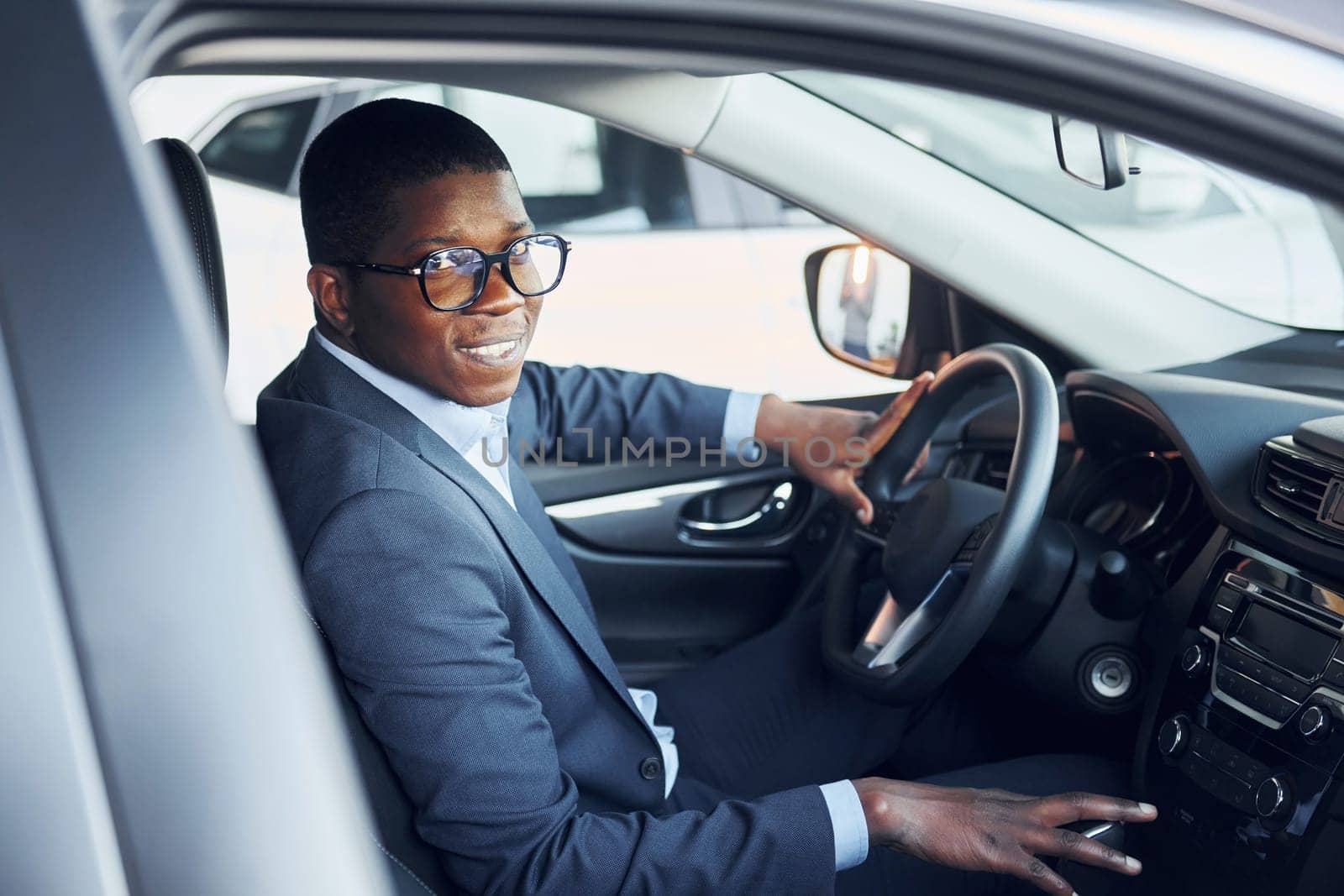 Side view. Young african american businessman in black suit is in the automobile.